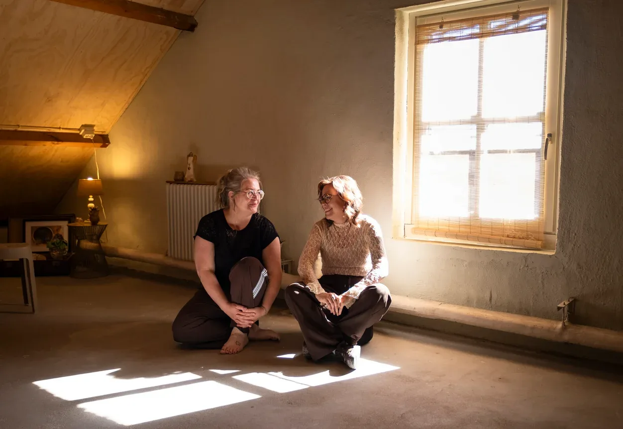 Twee vrouwen zitten op de grond in een kamer met een raam.